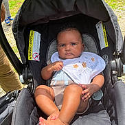Jalaiyah joined the competition — help win amazing prizes! baby, stroller, infant, outdoor, grass, bib, clothing, foot, person, child, sunlight, seat, black, cute, serious, animal_design, legs, hand, head, park