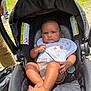 baby, stroller, infant, outdoor, grass, bib, clothing, foot, person, child, sunlight, seat, black, cute, serious, animal_design, legs, hand, head, park