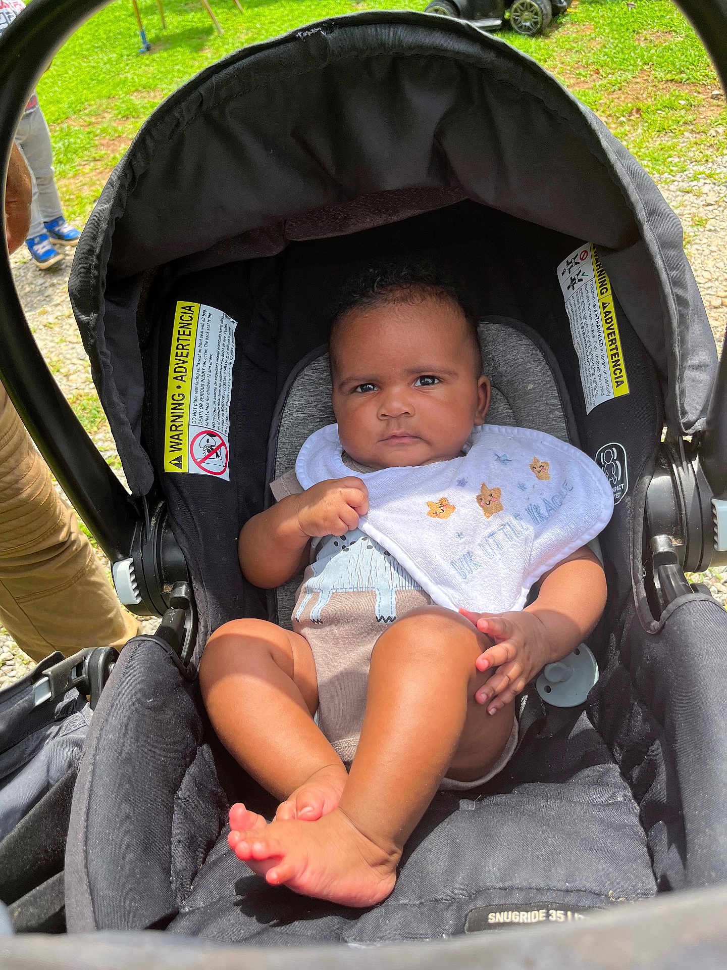 Jalaiyah joined the competition — help win amazing prizes! baby, stroller, infant, outdoor, grass, bib, clothing, foot, person, child, sunlight, seat, black, cute, serious, animal_design, legs, hand, head, park