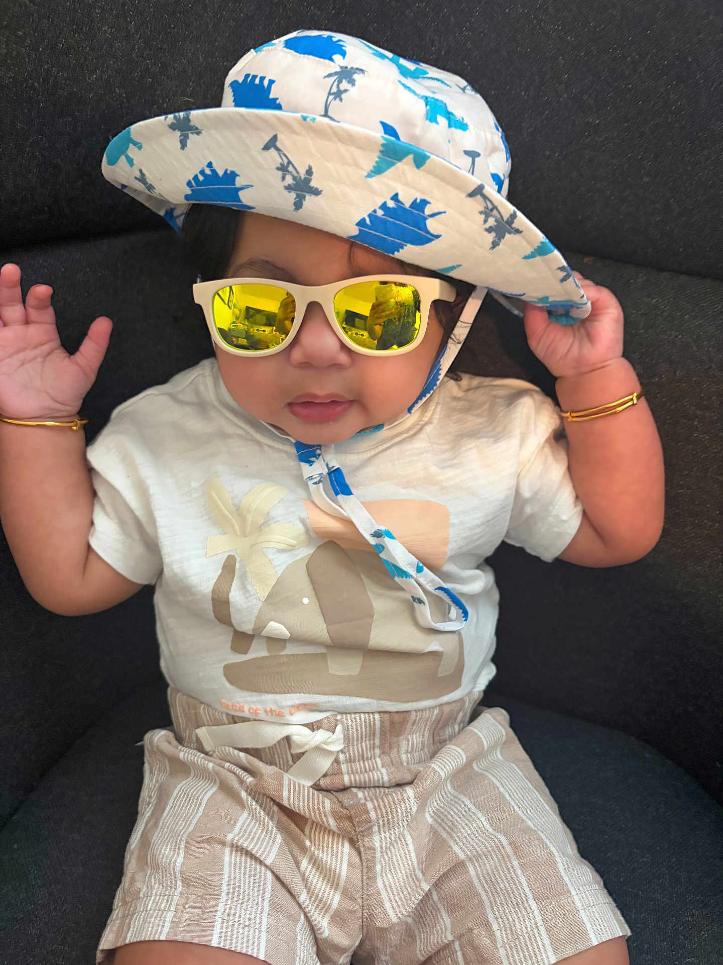 Reyaansh joined the competition — help win amazing prizes! baby, toddler, sunglasses, hat, bucket_hat, bracelet, gold_bangle, tshirt, shorts, striped_shorts, patterned_hat, reflection, face, portrait, seated, couch, accessories, summer, cute, neutral_expression