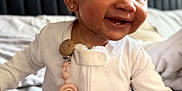 Zaria is registered to the contest to win money with this photo: baby, child, smile, curly_hair, pajamas, indoor, bedroom, pacifier_clip, rainbow, earring, happy, sitting, face, cute, infant, skin, person, clothing, closeup, portrait