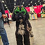 Nikita joined the competition — help win amazing prizes! dog, black_dog, white_fur, curly_fur, glasses, christmas_glasses, holiday, indoor, convention, leash, person, jeans, boots, vendor_booth, colorful, floor, lights, fur, pet, animal