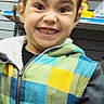 casual_wear, child, clothing, colorful_clothing, curly_hair, cute, expression, happy, hoodie, indoor, person, playful, portrait, retail, shelf, smile, standing, toy, toy_store, young_child