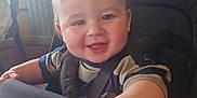 Theo is registered to the contest to win money with this photo: baby, child, high_chair, smiling, indoor, table, napkin, person, face, hand, clothing, seatbelt, hair, furniture, window, daylight, happy, cute, infant, restaurant