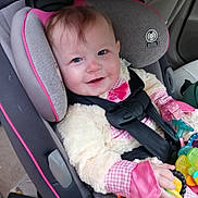 Allison is registered to the contest to win money with this photo: baby, car_seat, child, toy, pink_clothing, seat_belt, smiling, indoor, car_interior, blue_eyes, plush_jacket, hand, face, person, infant, safety_harness, cute, seat, child_safety, happy