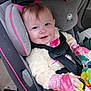baby, car_seat, child, toy, pink_clothing, seat_belt, smiling, indoor, car_interior, blue_eyes, plush_jacket, hand, face, person, infant, safety_harness, cute, seat, child_safety, happy