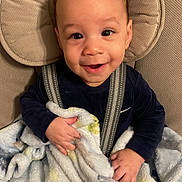 Elias is registered to the contest to win money with this photo: baby, smiling, blanket, baby_seat, child, happy, face, infant, cozy, comfort, cute, clothing, indoor, person, seatbelt, soft, patterned_blanket, portrait, young_child, sitting