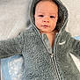 Elias is registered to the contest to win money with this photo: baby, child, infant, hooded_jacket, gray_jacket, fur_texture, lying_down, face, eyes, expression, soft_surface, cute, warm_clothing, portrait, young_child, zipper, indoor, skin, person, closeup