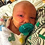 Isabella is registered to the contest to win money with this photo: baby, newborn, pacifier, blanket, medical_tape, face, infant, close_up, person, resting, indoor, floor, legs, clothing, patterned_fabric, comfort, child, swaddled, skin, head