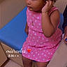 child, girl, pink_dress, sneakers, curly_hair, bow, blue_bench, indoor, tile_floor, jewelry, bracelet, necklace, sitting, thoughtful, portrait, casual_clothing, person, young_child, happy, cute