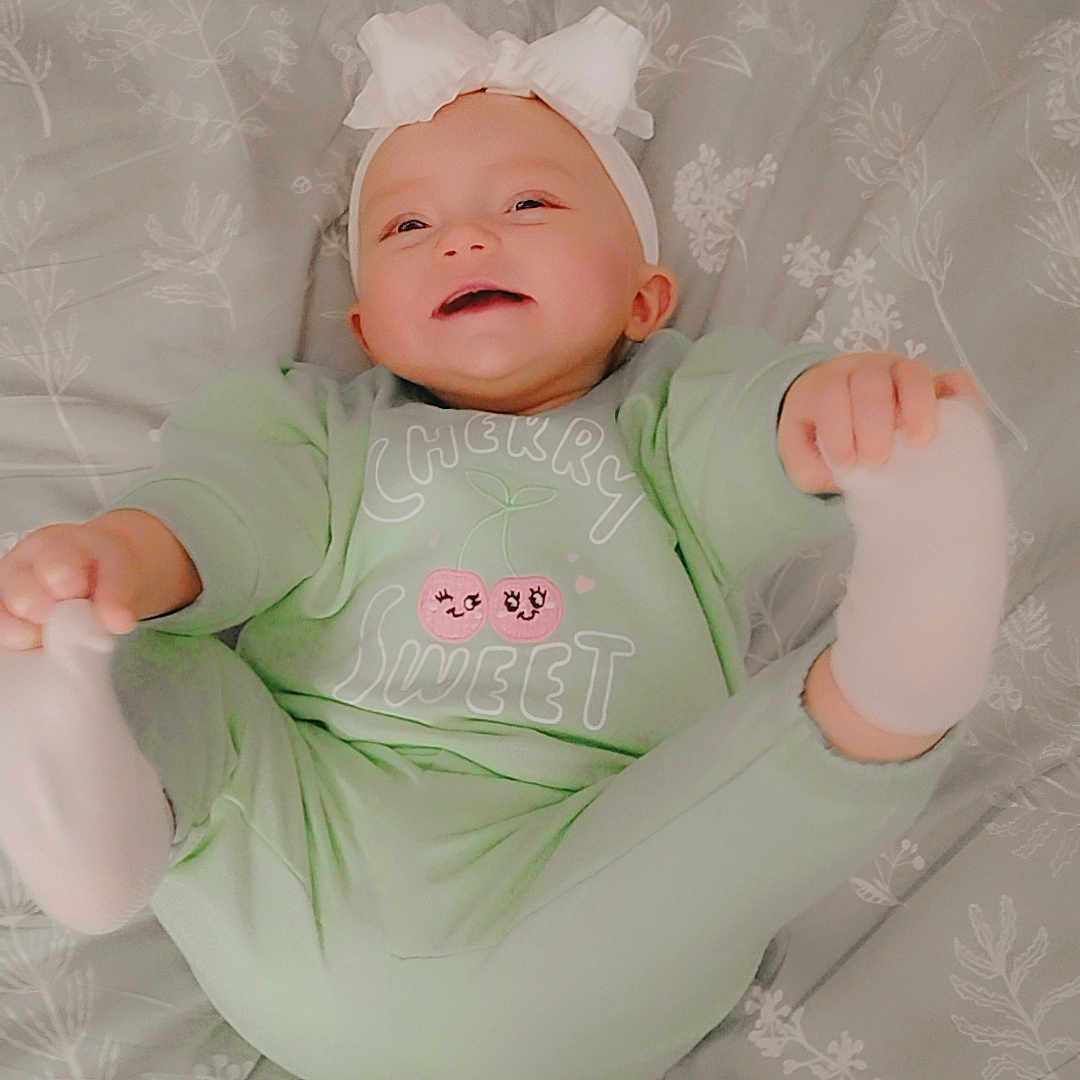 Kingsley is registered to the contest to win money with this photo: baby, bed, blanket, bow, child, comfort, cute, floral, green_clothing, happy, headband, indoors, infant, lying_down, pattern, person, playful, smiling, socks, soft_lighting