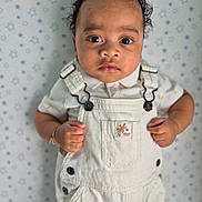 Aiden participe au concours pour gagner de l'argent avec cette photo : baby, child, overalls, white_clothing, curly_hair, bracelet, portrait, indoor, star_pattern, background, cute, young_child, skin, face, eyes, hands, fashion, infant, standing, expression
