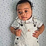 Aiden a rejoint le concours — aidez-le/la à gagner de superbes lots ! baby, child, curly_hair, white_overalls, short_sleeve_shirt, bracelet, star_pattern_background, indoor, portrait, standing, cute, young_child, skin, face, eyes, hands, clothing, fashion, soft_light, expression