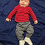 baby, infant, child, striped_shirt, red, gray_pants, cargo_pants, white_sneakers, footwear, blanket, blue_blanket, laying_down, smiling, face, hands, cute, indoors, casual_clothing, small_feet, young
