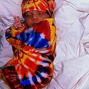 Sophia is registered to the contest to win money with this photo: baby, sleeping, peace_sign, tie_dye, blanket, hat, colorful, infant, bed, bedding, cute, peaceful, wrapped, soft, newborn, child, portrait, cozy, rest, warm