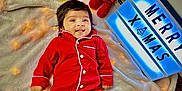 Swaha is registered to the contest to win money with this photo: baby, child, pajamas, red_clothing, blanket, christmas_tree, santa_claus_figure, lantern, lightbox, holiday, festive, smiling, indoor, floor, decorations, cozy, soft_texture, celebration, cute, portrait