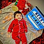 baby, child, pajamas, red_clothing, blanket, christmas_tree, santa_claus_figure, lantern, lightbox, holiday, festive, smiling, indoor, floor, decorations, cozy, soft_texture, celebration, cute, portrait