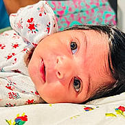 Swaha is registered to the contest to win money with this photo: baby, newborn, infant, face, eyes, floral, blanket, clothing, cute, lying_down, skin, hair, portrait, closeup, soft, child, adorable, sleeping_area, patterned, young