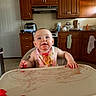 appliance, baby, bib, cabinet, child, countertop, face, food, hand, happy, high_chair, indoor, kitchen, messy, person, refrigerator, sink, smile, table, towel