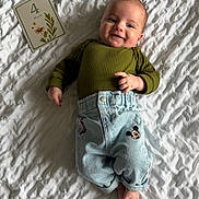 Tiago a rejoint le concours — aidez-le/la à gagner de superbes lots ! baby, infant, smiling, lying_down, clothing, green_top, blue_pants, mickey_mouse, milestone_card, white_blanket, texture, face, hands, feet, cute, child, indoors, portrait, happy, person