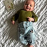baby, infant, smiling, lying_down, clothing, green_top, blue_pants, mickey_mouse, milestone_card, white_blanket, texture, face, hands, feet, cute, child, indoors, portrait, happy, person