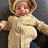 baby, child, hoodie, beige, smile, tongue_out, knitted_hat, cute, playful, person, clothing, fabric, dark_background, portrait, infant, sitting, warm, casual, face, indoors