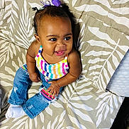 Ailani joined the competition — help win amazing prizes! child, baby, toddler, portrait, smiling, sitting, bed, bedspread, patterned_background, rainbow_top, striped_clothing, jeans, bow, hair_accessory, earrings, socks, indoor, happy, fashion, close_up
