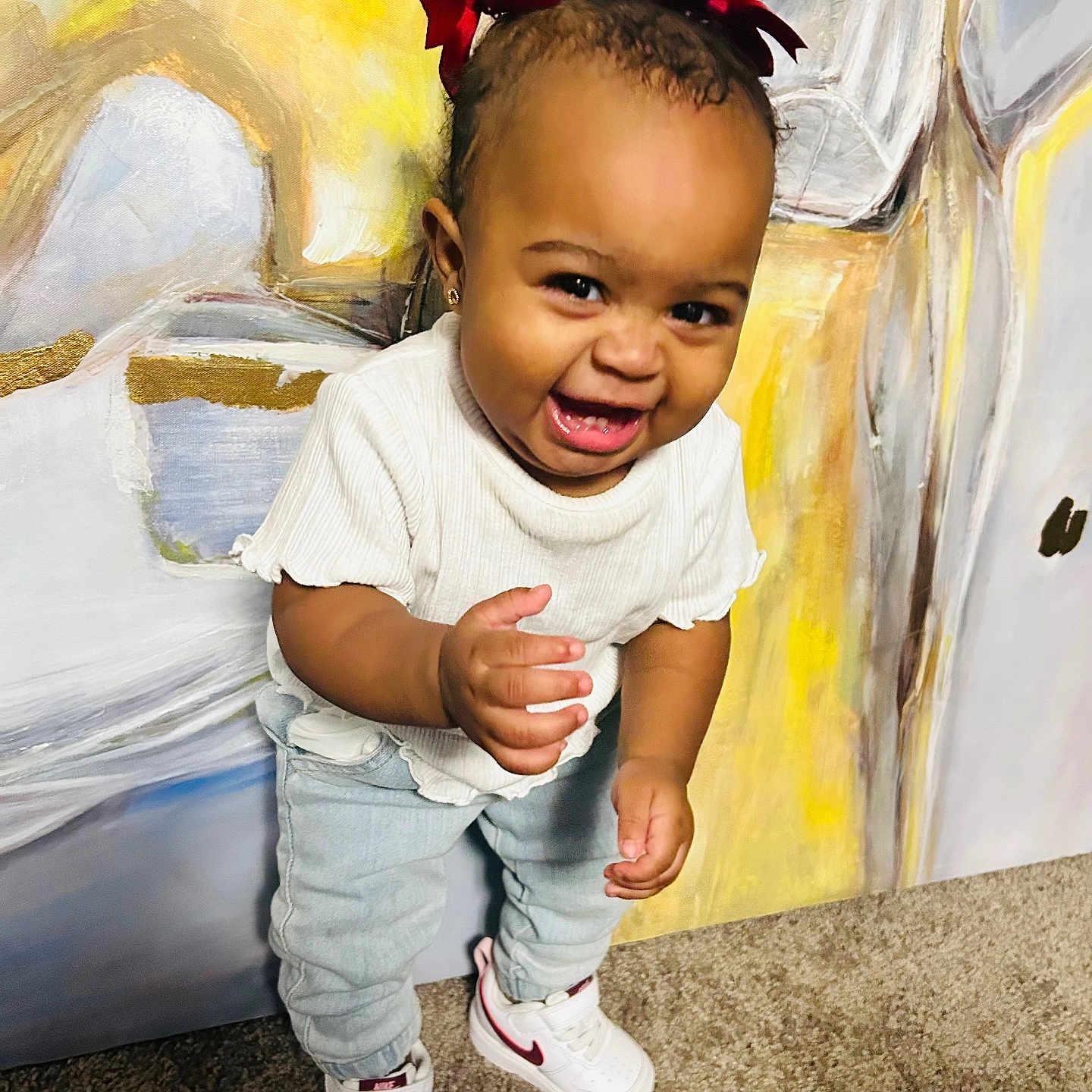 Ailani is registered to the contest to win money with this photo: baby, child, toddler, girl, portrait, smiling, happy, laughing, standing, face, red_bow, hair, white_shirt, jeans, sneakers, indoors, carpet, abstract_background, colorful, photography