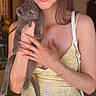 woman, glasses, kitten, cat, yellow_dress, indoor, handbag, smile, long_hair, jewelry, bracelet, ring, holding, posing, cute, pet, furniture, door, portrait, light