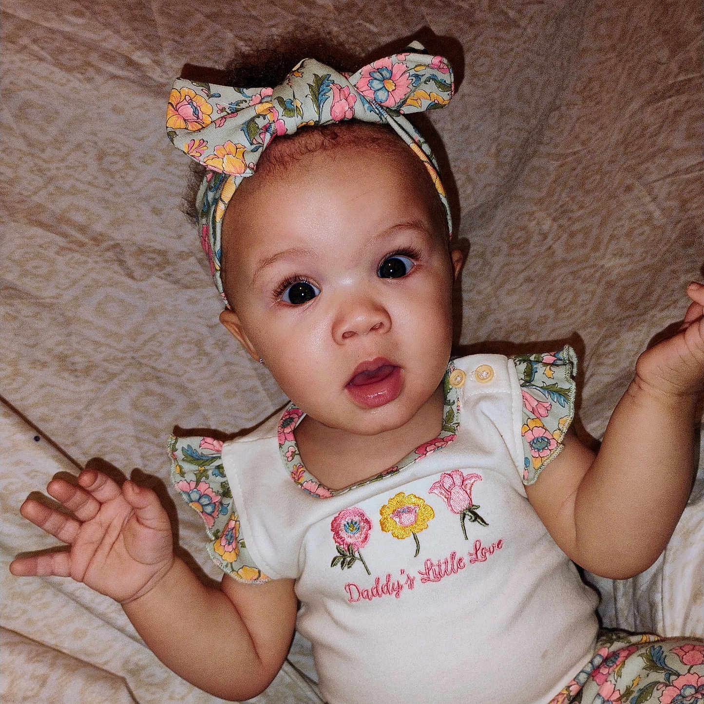 Antania joined the competition — help win amazing prizes! baby, big_eyes, blanket, bow, child, clothing, cute, embroidered_text, eyelashes, floral_pattern, hands, headband, indoor, infant, mouth_open, onesie, patterned_pants, portrait, sitting, surprised_expression