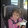 car, car_seat, casual_clothing, child, communication, daytime, face, girl, glasses, happy, person, pink_sweater, screen, seatbelt, smiling, snack, technology, vehicle_interior, video_call, window