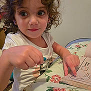 Scarlett joined the competition — help win amazing prizes! activity, bedspread, casual_clothing, child, closeup, crayon, curly_hair, cute, education, floral_pattern, girl, indoor, learning, person, playful, pointing, smiling, white_shirt, workbook, young