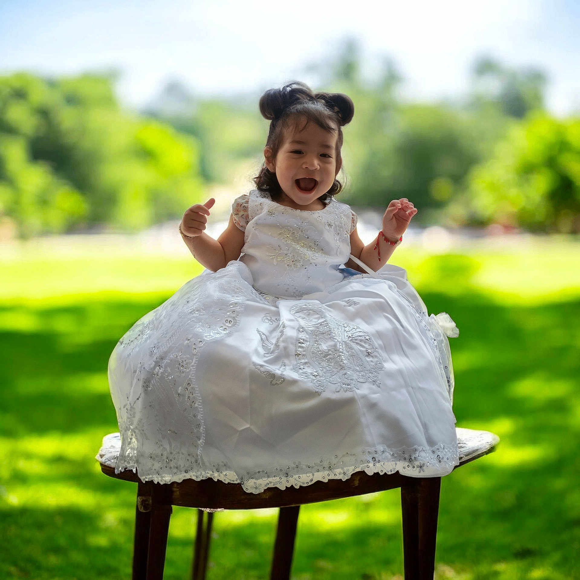 Sophia joined the competition — help win amazing prizes! child, toddler, smiling, white_dress, outdoor, greenery, grass, wooden_stool, happy, portrait, sunlight, nature, cute, sitting, hair_buns, daylight, young_child, celebration_dress, joyful, person