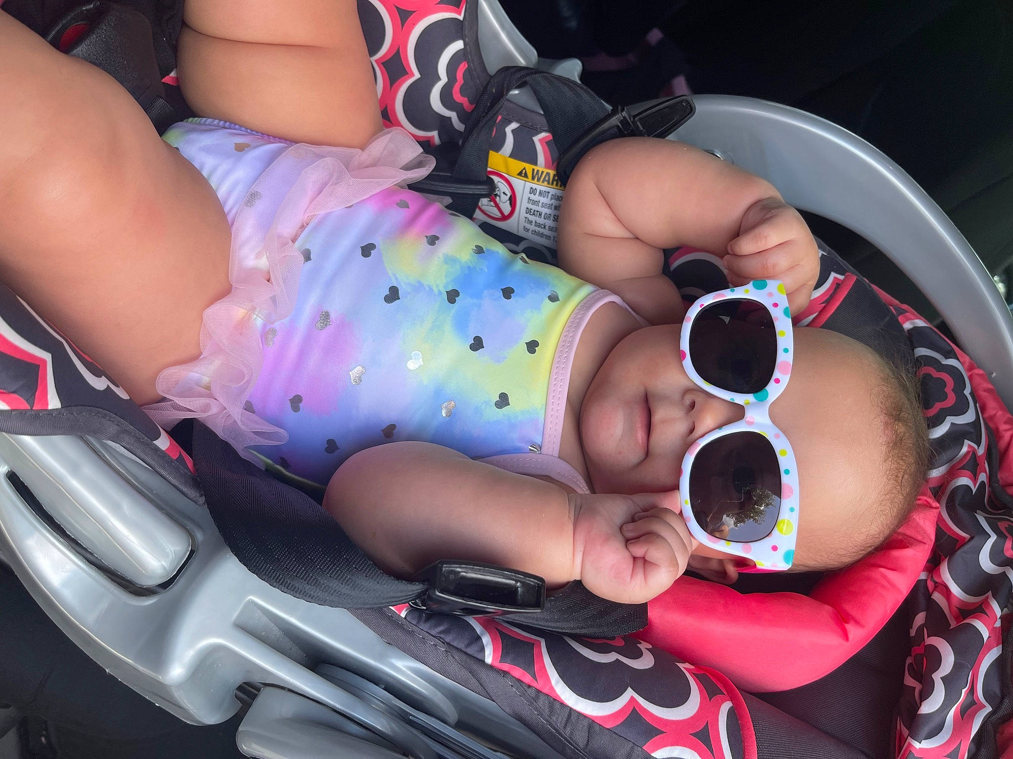 Aliyah is registered to the contest to win money with this photo: arm, auto_part, automotive_design, baby, baby_products, baby_toddler_clothing, car_seat, child, eyewear, goggles, hand, human_leg, mouth, nail, pattern, person, pink, sunglasses, thigh, toddler