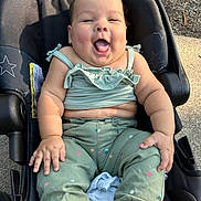 Mia joined the competition — help win amazing prizes! baby, child, infant, smiling, laughing, sitting, car_seat, outdoor, sunlight, portrait, face, happy, clothing, green_outfit, pink_sandal, star_pattern, playful, roadside, daylight, photography