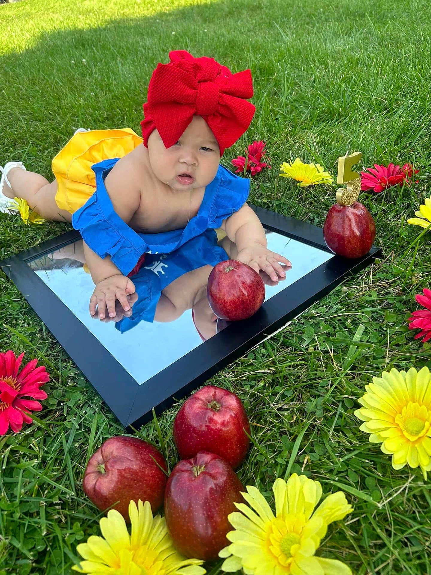 Mía Lsabella joined the competition — help win amazing prizes! baby, child, mirror, grass, red_bow, blue_clothing, yellow_clothing, red_apples, flowers, yellow_flowers, red_flowers, outdoor, nature, reflection, celebration, number_5, cute, infant, summer, playful