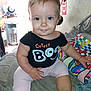 baby, toddler, child, sitting, black_shirt, pink_pants, couch, pillow, indoor, face, smile, person, curly_hair, foot, hand, colorful, clothing, cute, expression, home