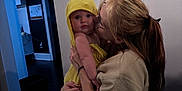 Adalee is registered to the contest to win money with this photo: baby, child, woman, indoor, hug, kiss, yellow_towel, hooded_towel, curious, affection, person, clothing, long_hair, light_skin, face, holding, wall, home, love, candid