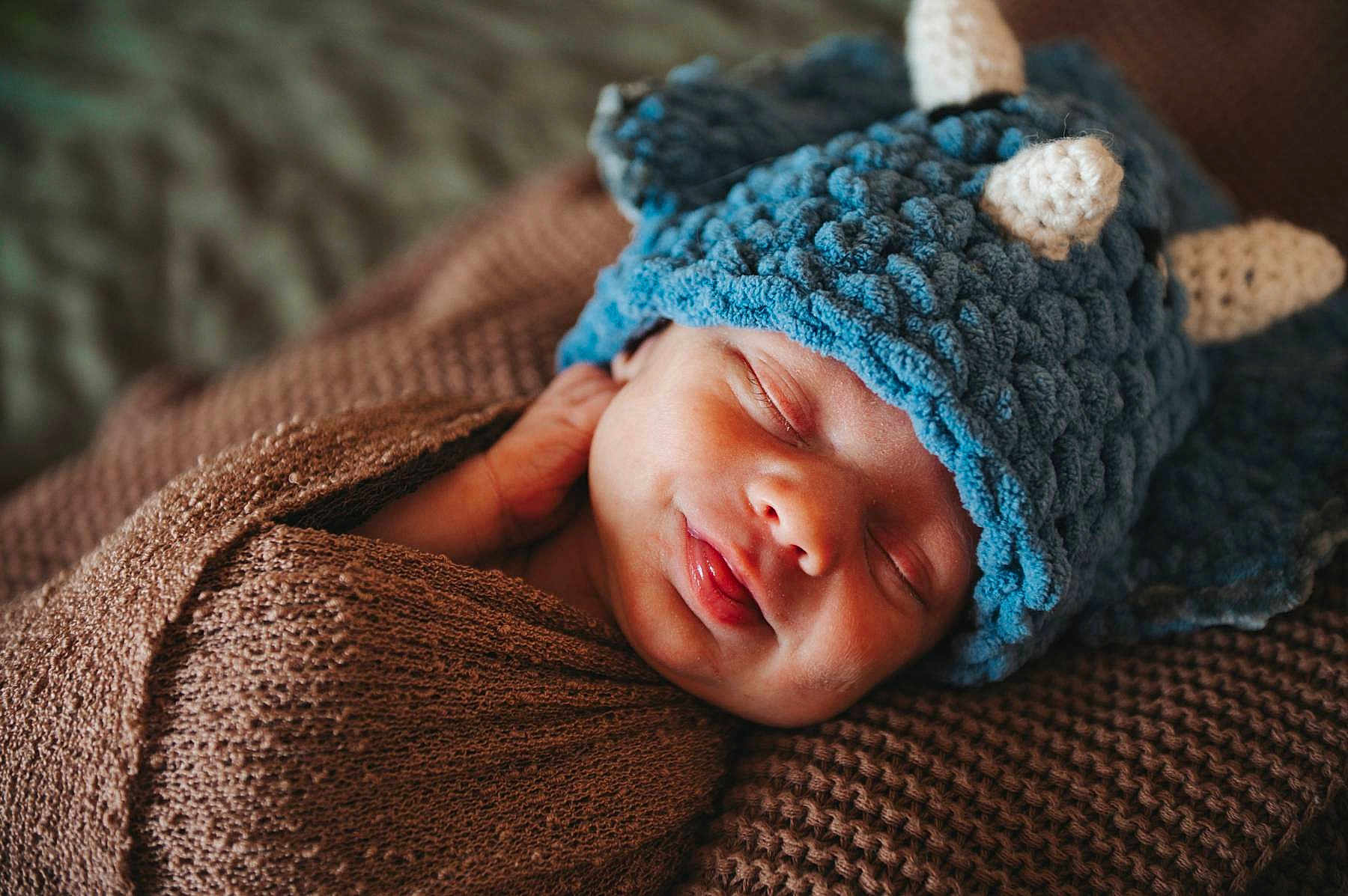 Milo joined the competition — help win amazing prizes! baby, newborn, sleeping, hat, knit_hat, blue_hat, blanket, brown_blanket, swaddle, cozy, portrait, closeup, peaceful, infant, sleeping_baby, adorable, tongue_out, knitted_texture, fabric, newborn_photography