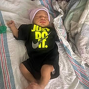 Larry is registered to the contest to win money with this photo: newborn, baby, infant, sleeping, onesie, hat, blanket, hospital, clothing, foot, hand, face, person, laying_down, text_on_clothing, pacifier, striped_blanket, soft_lighting, cute, indoors