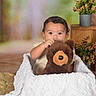 child, toddler, portrait, teddy_bear, stuffed_animal, blanket, baby, sitting, indoor, home, nursery, flowers, plants, wooden_furniture, cozy, cute, looking_at_camera, brown_bear, white_blanket, photography