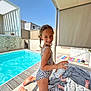 child, baby, swimsuit, pool, outdoor, sunny, smiling, blanket, spray_can, deck, shade, modern, playful, summer, water, person, foot, happy, toddler, candid