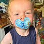 Enver is registered to the contest to win money with this photo: toddler, child, pacifier, curly_hair, indoor, playroom, toys, blue_shirt, face, portrait, smile, baby, person, young_child, home, candid, cute, expression, funny, childhood