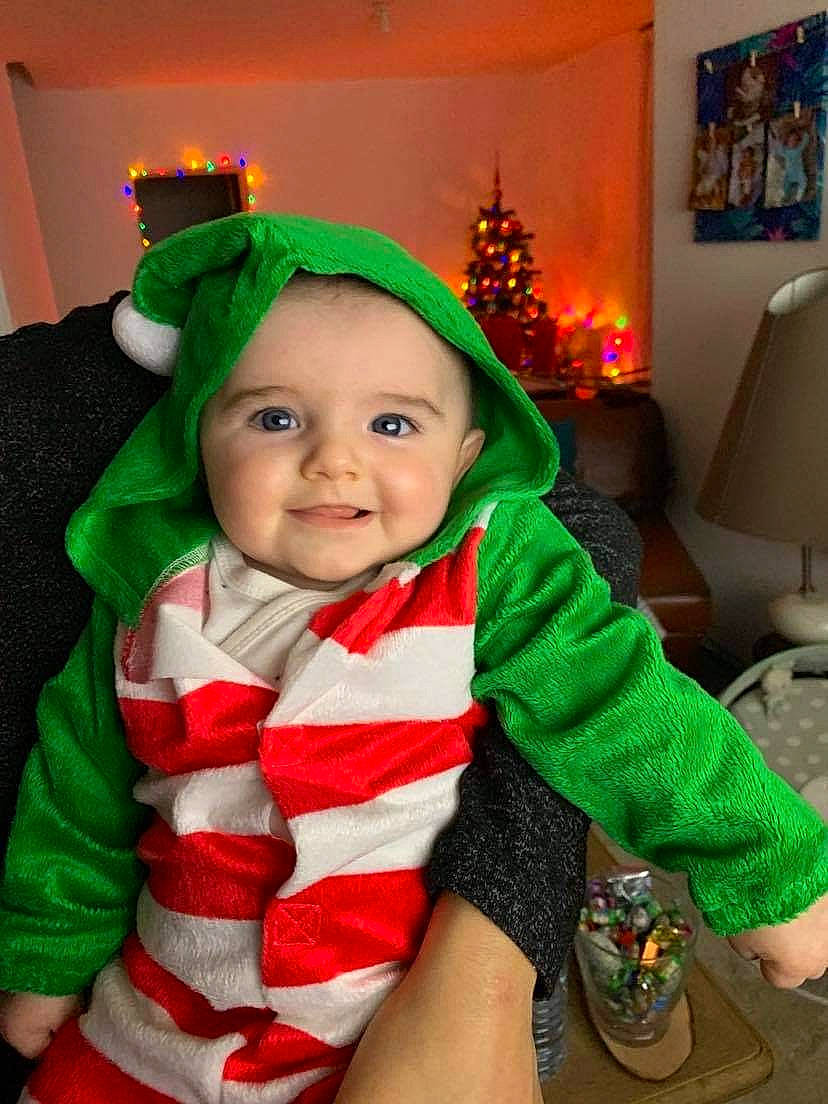 Nathan participe au concours pour gagner de l'argent avec cette photo : baby, baby_toddler_clothing, child, christmas, christmas_decoration, christmas_eve, christmas_ornament, costume, costume_accessory, costume_hat, event, fictional_character, green, headwear, holiday, interior_design, joy, lamp, lighting, person