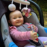 Rose a rejoint le concours — aidez-le/la à gagner de superbes lots ! baby, car_seat, toy, pink_clothing, smiling, child, outdoor, greenery, soft_toy, happy, infant, sitting, playful, cute, person, seatbelt, nature, daylight, face, closeup