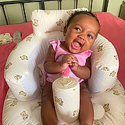 Jade is registered to the contest to win money with this photo: baby, infant, smiling, pink_clothing, seat, teddy_bear_pattern, cushion, bed, bottle, wipes, happy, person, indoor, cute, child, small, skin, feet, hands, head