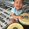 baby, bongo, child, drums, face, happy, indoor, infant, living_room, musical_instrument, percussion, photography, play_walker, portrait, rug, short_hair, sitting, smiling, striped_shirt, toy