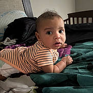 Darius is registered to the contest to win money with this photo: baby, infant, bed, striped_shirt, diaper, curious, looking_back, indoor, child, person, furniture, blanket, head, skin, cute, young, sleepwear, room, photography, portrait