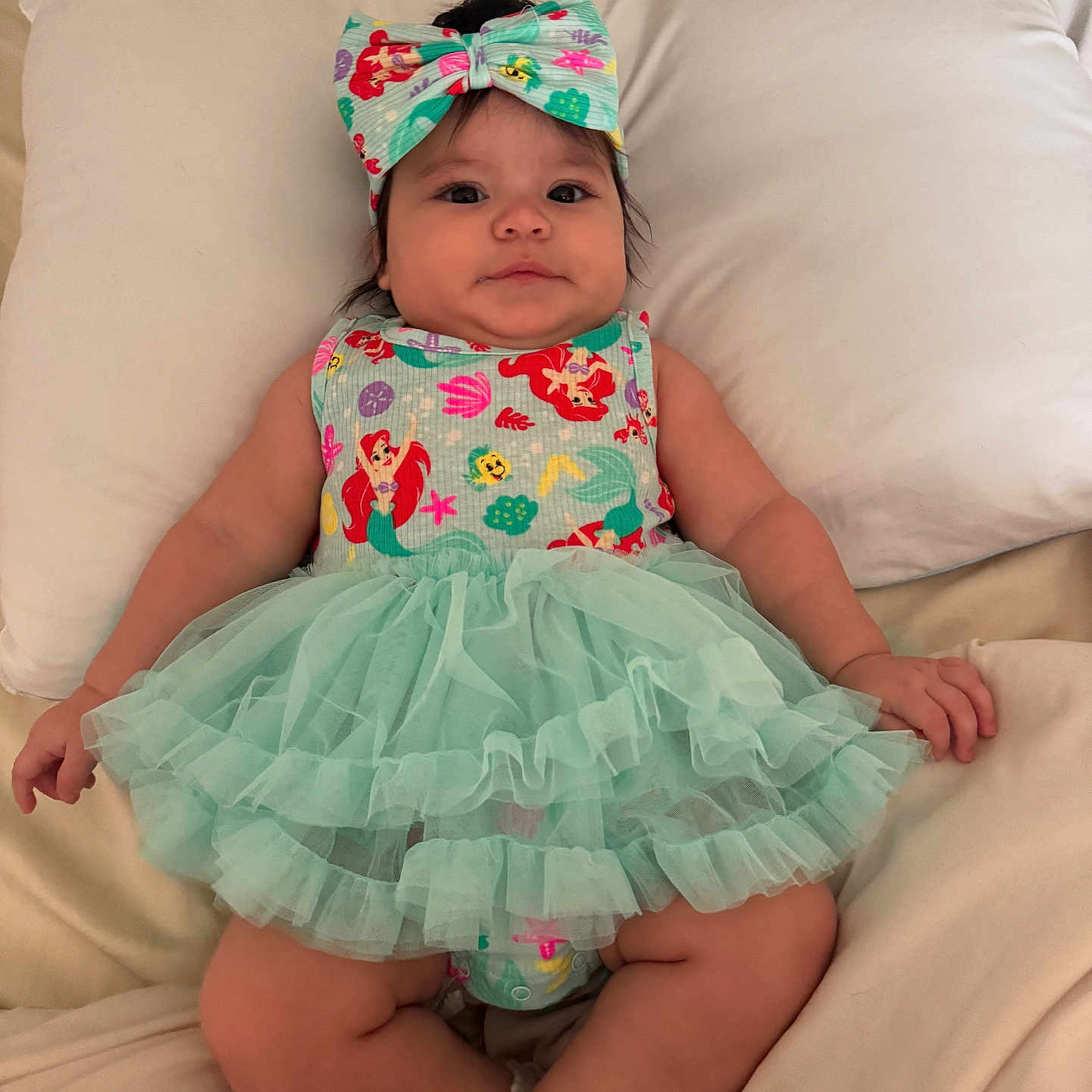 Auriel is registered to the contest to win money with this photo: baby, bed, blanket, bow, child, clothing, cute, dress, fabric, headband, indoors, infant, legs, person, pillow, skin, smile, socks, soft, tutu
