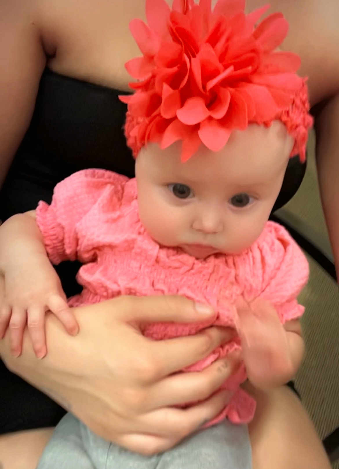 Ameiire is registered to the contest to win money with this photo: baby, child, headband, flower, pink_clothing, adult_hand, holding, cute, infant, portrait, indoor, person, skin, face, eyes, hands, sitting, clothing, closeup, soft